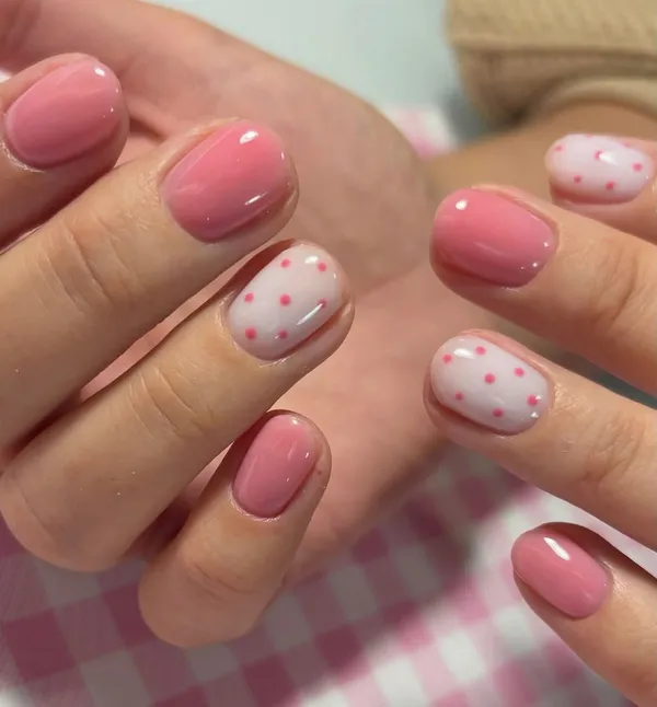 Uñas cortas en rosa con lunares fucsia sobre un mantel de cuadros