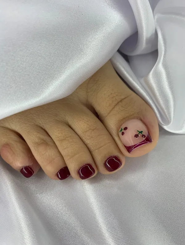 Pedicure en tono vino con cerezas pintadas a mano en el dedo gordo