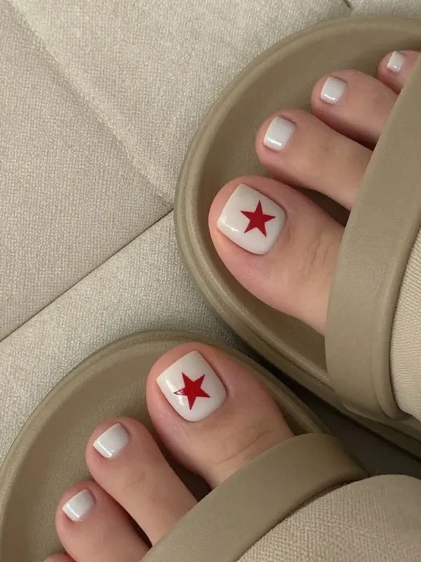 Pedicure blanca con una estrella roja pintada en cada dedo gordo